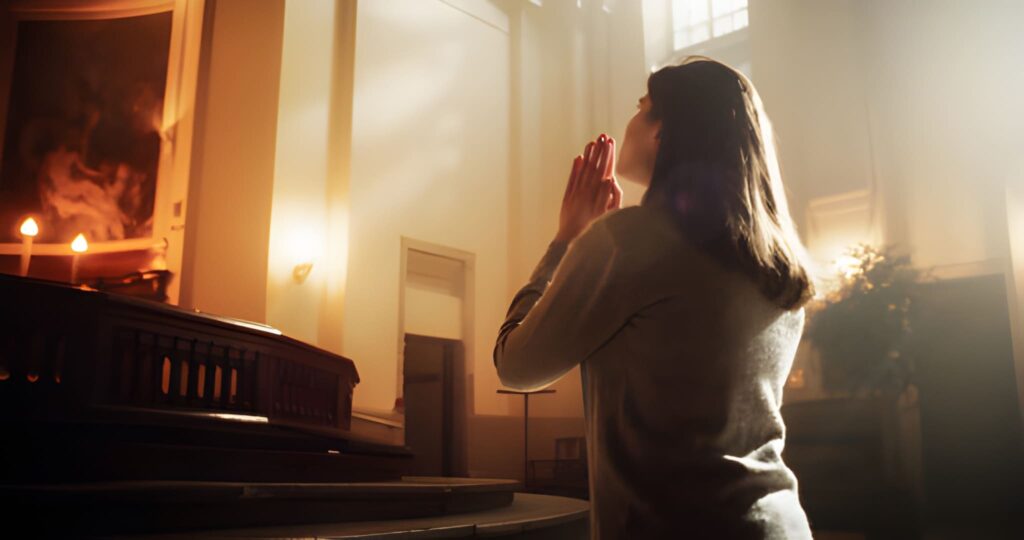 A girl kneeling in church with her hands clasped in prayer and head tilted upwards