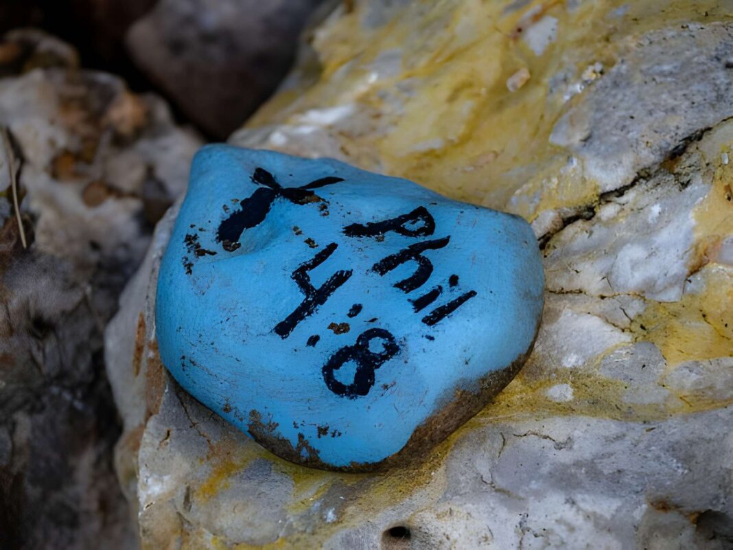 A painted rock in a garden with a Bible Verse, Philippians 4:8