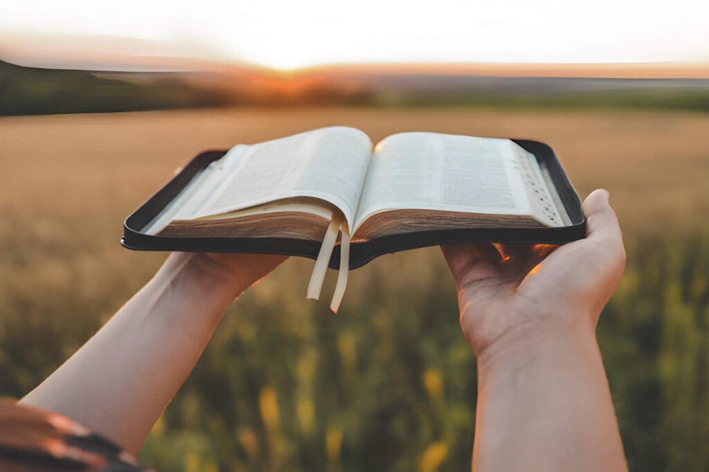 Hands holding a bible above an open field with its pages open