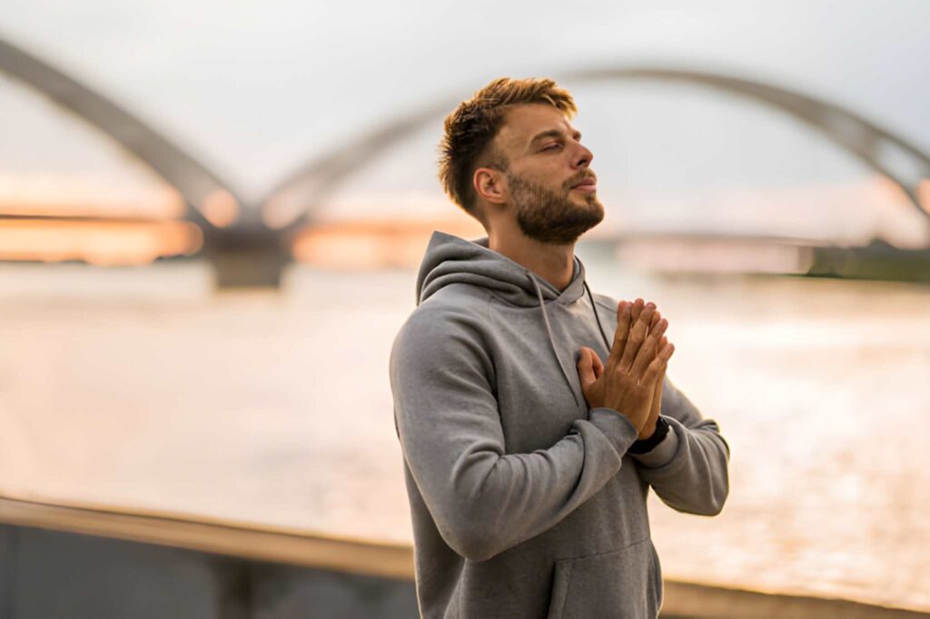 An athletic man relaxing his mind, head facing upwards, with eyes closed and both hands clapped in front of his chest - Image: iStockphoto