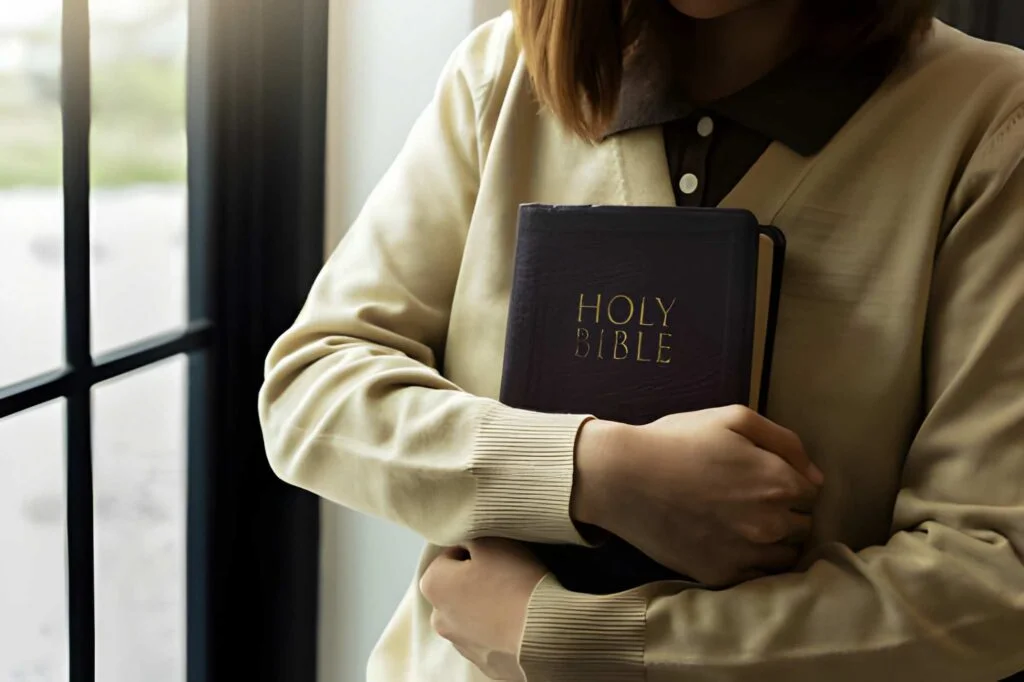 Young woman praying to God with the bible, holding the bible to her chest