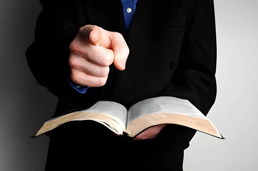 A minister holding an open Bible and pointing at you.