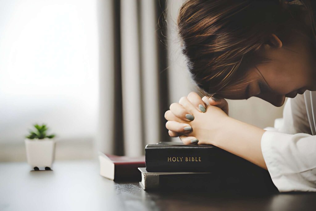 A woman praying with a bible on the table